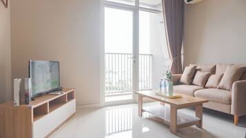 A modern living room with a flat-screen TV on a wooden stand, a beige sofa, a wooden coffee table, and a large window with curtains.