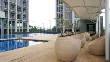 A modern outdoor pool area with a wooden deck, lounge chairs, and a covered seating area.