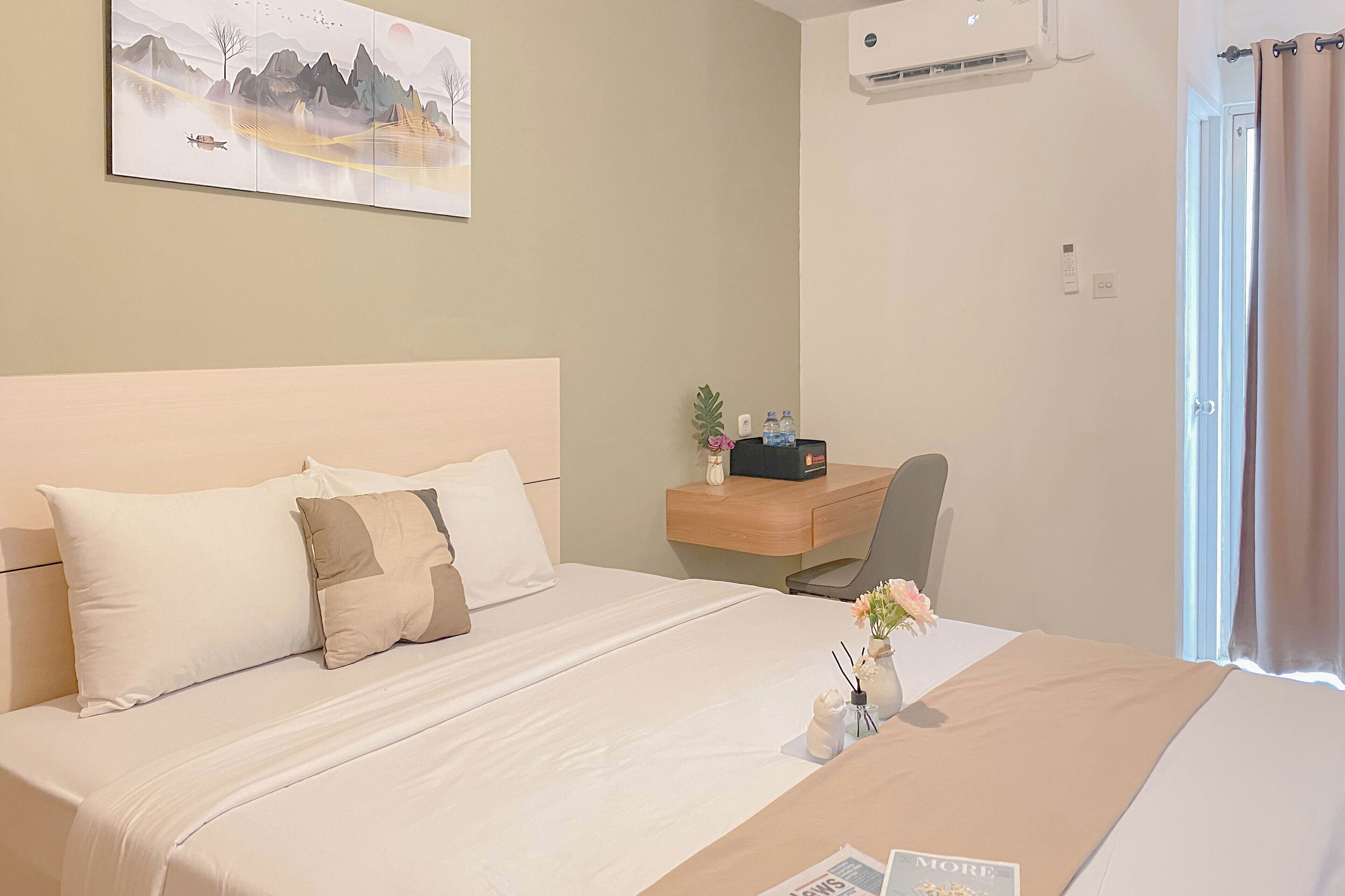 Une chambre d’hôtel comprenant un lit, un bureau, une chaise, une petite table avec un vase de fleurs et un climatiseur fixé au mur.