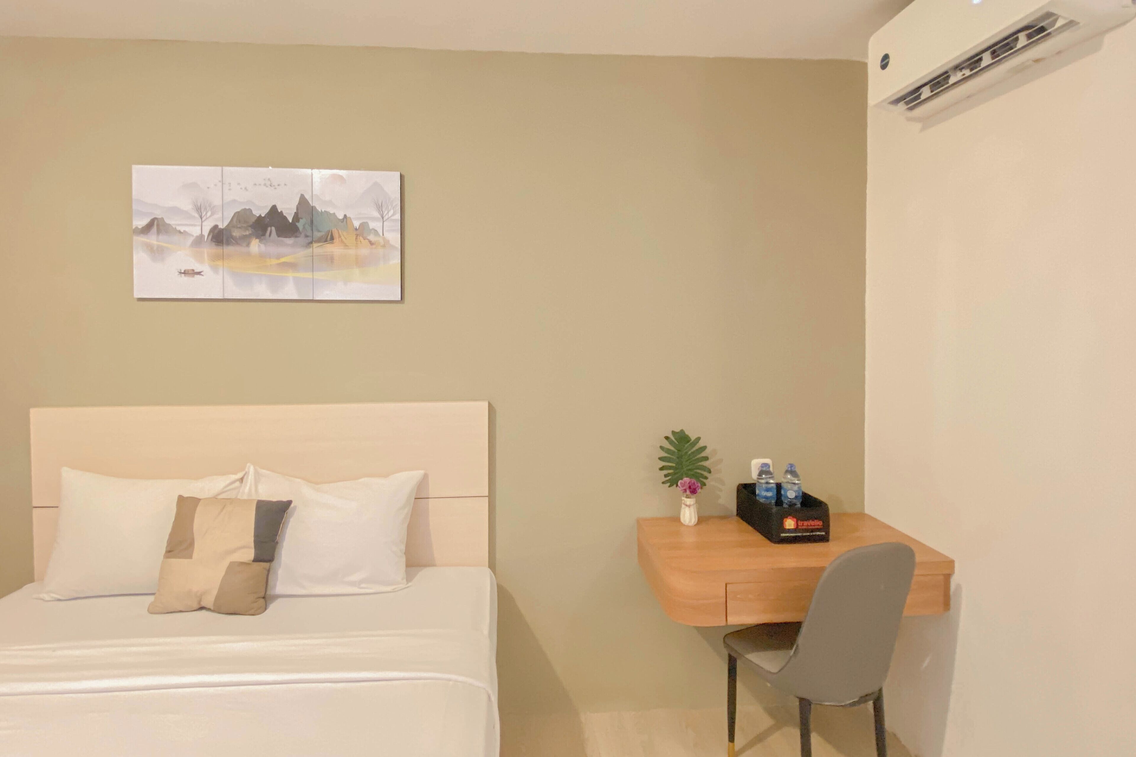 Une chambre d’hôtel comprenant un lit, un bureau avec une chaise, une petite plante et une bouteille d’eau.