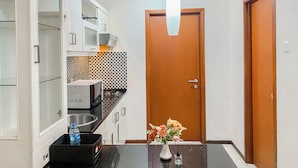 A kitchen with white cabinets, a microwave, and a sink. There is a wooden door and a vase with flowers on the counter. - Good Deal And Restful 1Br At Apartment Thamrin Residence (Jakarta)