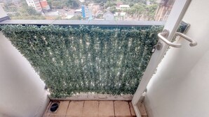 Un balcón con vista a un paisaje urbano, una barandilla de metal y un ventanal pequeño.