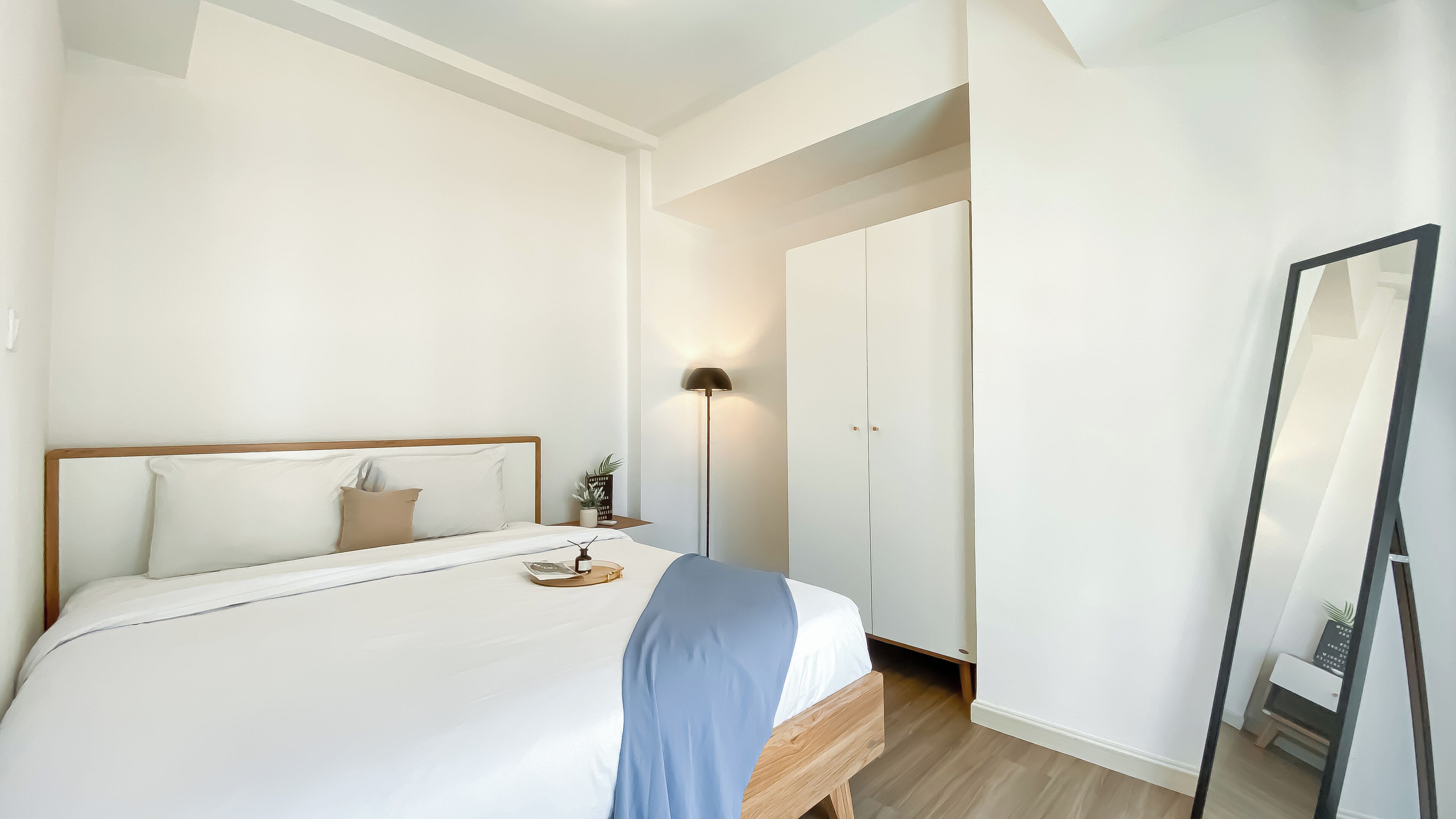 A neatly made bed with a wooden headboard, a bedside table with a lamp, and a wardrobe with a mirror.