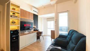 A modern living room with a flat-screen TV displaying 'NETFLIX', a sofa, a coffee table, and a kitchen area with a built-in oven and microwave. - Stunning And Spacious 1Br Apartment At Tokyo Riverside (Teluknaga)
