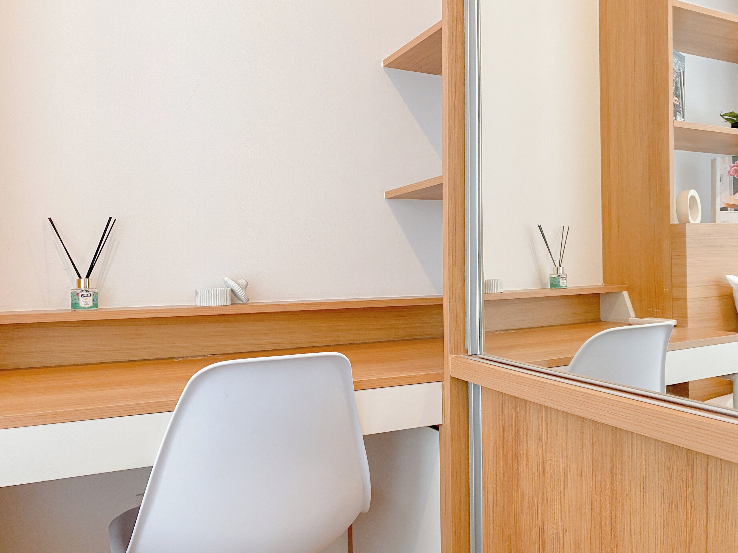 A modern, minimalist room with a wooden desk, white chairs, and a mirror reflecting the room.