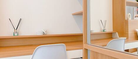 A modern, minimalist room with a wooden desk, white chairs, and a mirror reflecting the room.