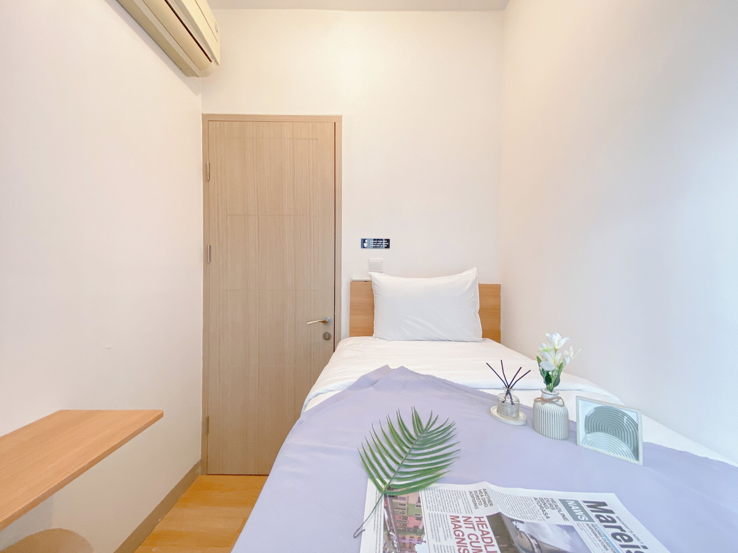 Hotellihuone, jossa on sänky, puuovi, pieni pöytä ja seinälle asennettu ilmastointilaite.