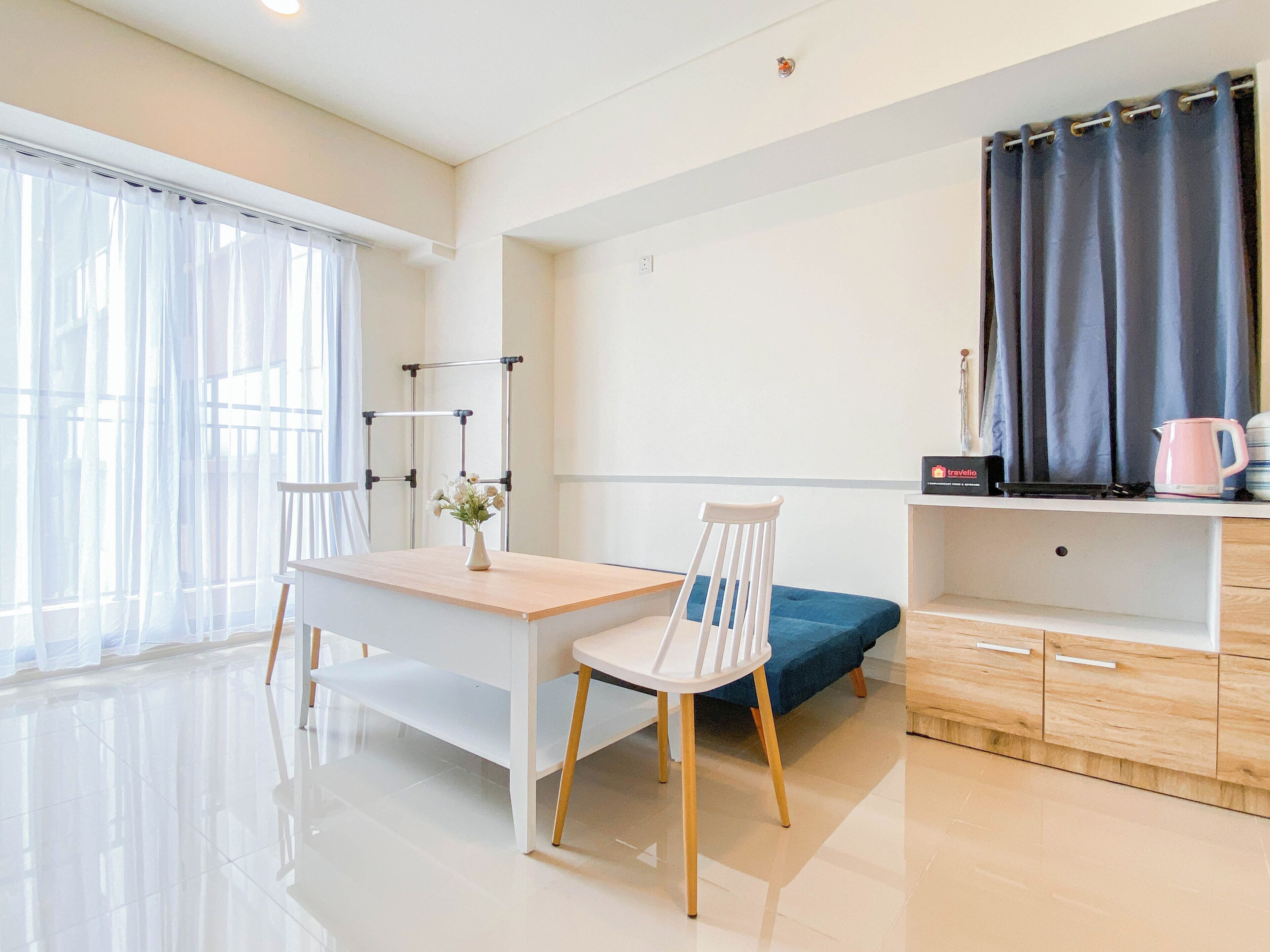 A modern, well-lit room with a wooden desk, a white chair, a blue sofa, and a small kitchenette area.