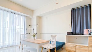 Una habitación moderna y luminosa con un escritorio de madera, una silla blanca, un sofá azul y una pequeña zona de kitchenette.
