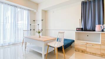 A modern, well-lit room with a wooden desk, a white chair, a blue sofa, and a small kitchenette area.