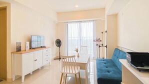 Una sala de estar moderna con un sofá, un televisor, una mesa de comedor con sillas, un ventilador y una ventana con cortinas.