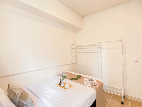 A hotel room with a bed, a small table with a vase and a tray, and a drying rack against the wall.