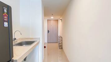 A narrow hallway with a sink and a refrigerator on the left, a door at the end, and a metal rack against the wall.