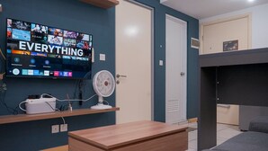 A modern living room with a flat-screen TV displaying a streaming service interface, a white fan, a wooden coffee table, and a grey sofa. - Comfortable And Strategic 2Br Apartment M-Town Residence (Gading Serpong)