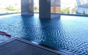 An indoor swimming pool with clear water, wooden deck, and a view of greenery outside. - Elegant And Compact 1Br At Grand Sungkono Lagoon Apartment (Surabaya)