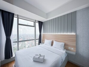 A modern hotel room with a large bed, a wooden headboard, and a city view through large windows. - Elegant And Compact 1Br At Grand Sungkono Lagoon Apartment (Surabaya)