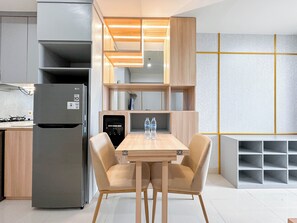 A modern kitchen with a built-in refrigerator, a water dispenser, and a wooden table with two chairs. - Elegant And Compact 1Br At Grand Sungkono Lagoon Apartment (Surabaya)