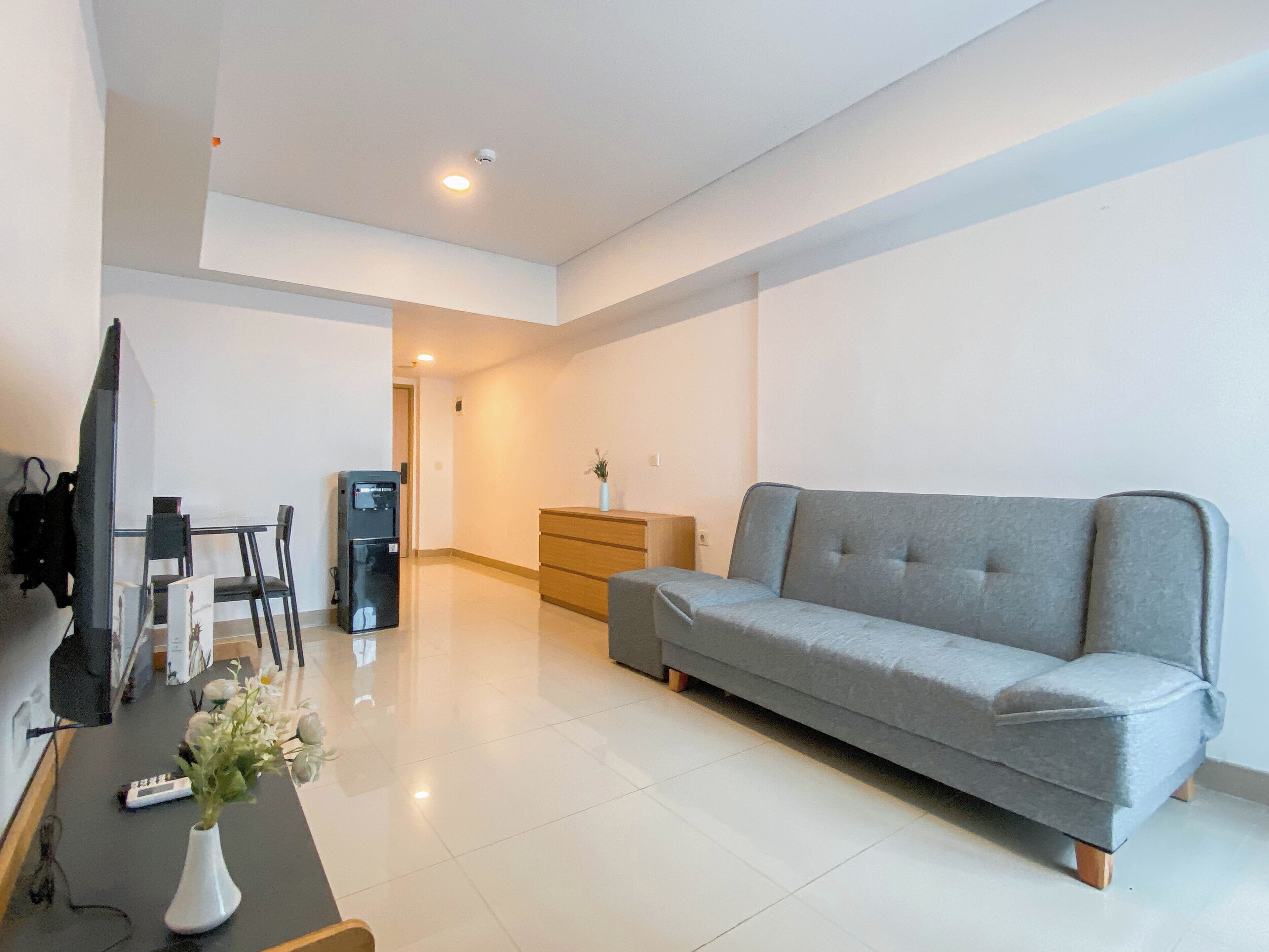 A modern living room with a grey sofa, a TV, a coffee machine, and a small table with a vase of flowers.