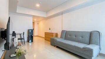 A modern living room with a grey sofa, a TV, a coffee machine, and a small table with a vase of flowers.