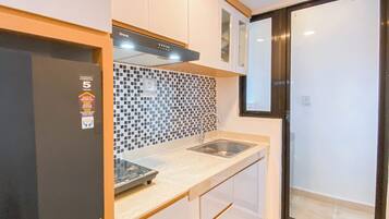 A compact kitchen with a black refrigerator, a tiled backsplash, a stainless steel sink, and white cabinets.