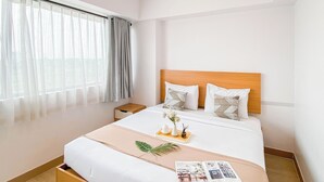 A hotel room with a bed, a nightstand, a window with curtains, and a bedside table with a tray of items. - Comfort And Simply Look 2Br At Meikarta Apartment (Cikarang)