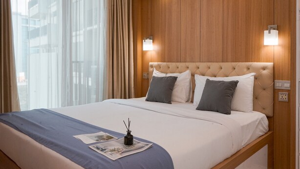 Ein Hotelzimmer mit einem großen Bett, einem hölzernen Kopfteil, zwei Wandleuchten und einem fenster mit Vorhängen.