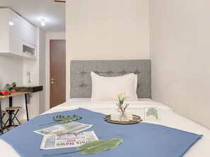 Habitación de hotel ordenada con una cama, una mesita de noche con una planta, un estante pequeño y una puerta.