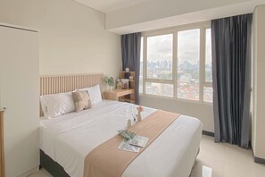 A hotel room with a large bed, a nightstand, a small table, and a window with curtains.