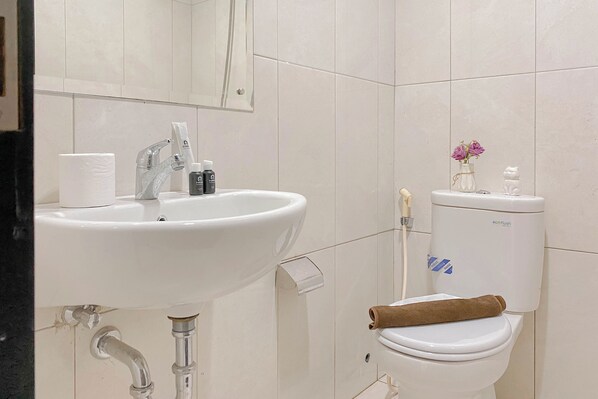 A bathroom with a white sink, mirror, toilet, and a towel on the toilet seat.