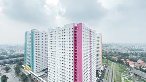 A high-rise building with multiple floors, a prominent pink section, and a view of the surrounding cityscape. - Best Price And Relaxing 1Br At Green Pramuka City Apartment (Jakarta)