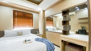 A modern hotel room with a large bed, a bedside table, a mirror, and a desk with a chair. - Best Price And Relaxing 1Br At Green Pramuka City Apartment (Jakarta)