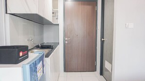 A compact kitchen with a wooden door, a sink, and a black box labeled "travelio" on the counter. - Cozy And Homey Studio At Riverdale Apartment (Cikarang)