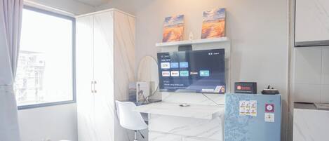 A hotel room with a bed, a desk with a computer, a blue refrigerator, and a window with curtains.