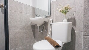 A bathroom with a toilet, sink, and a vase of flowers on the wall. - Cozy And Homey Studio At Riverdale Apartment (Cikarang)