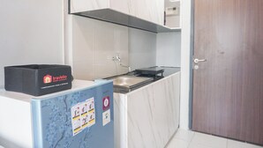A compact kitchen with a sink, a black box labeled 'Travelio Property Management', and a blue refrigerator with various stickers. - Cozy And Homey Studio At Riverdale Apartment (Cikarang)