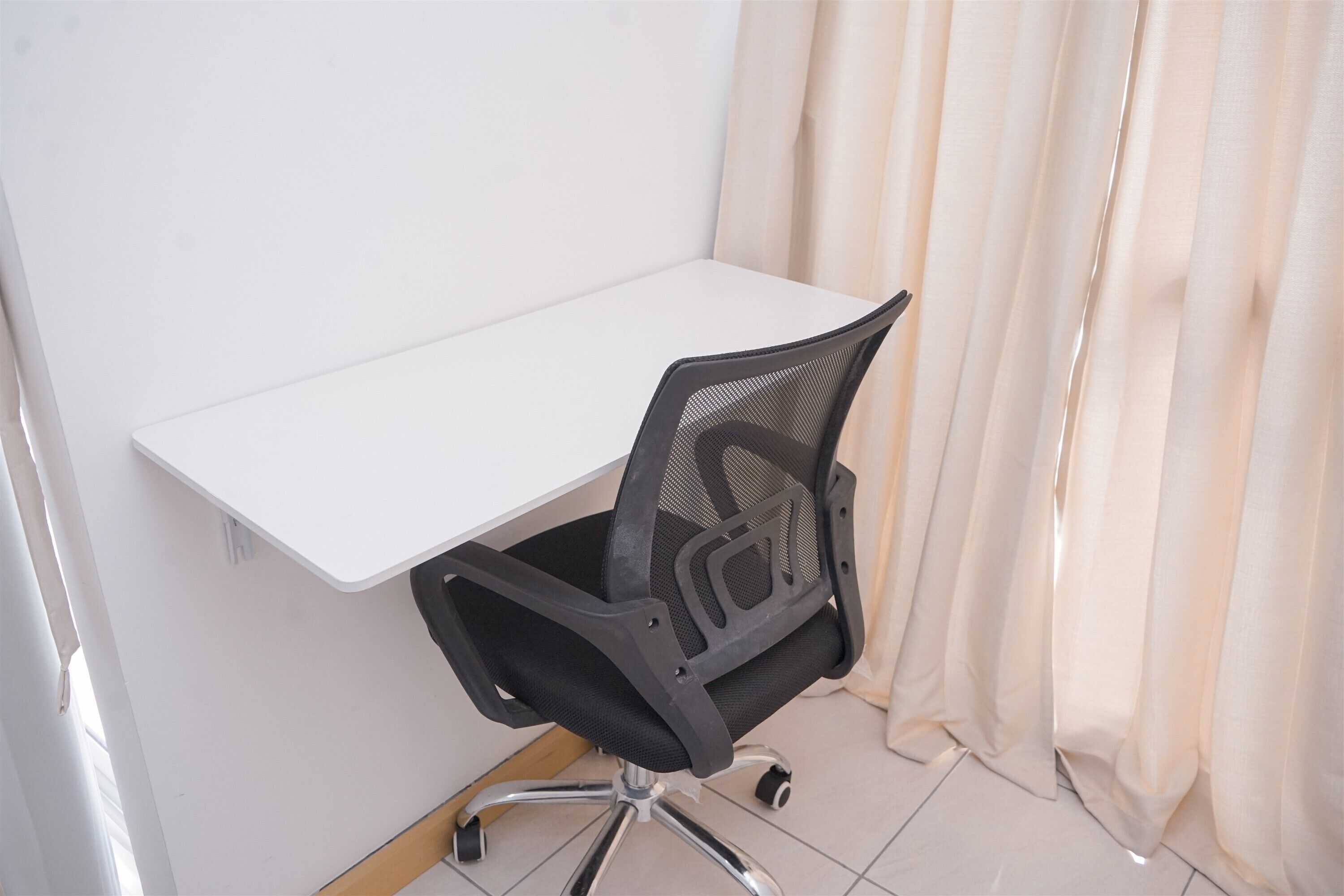 Un escritorio blanco con una silla de oficina de malla negra.