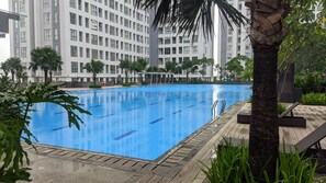 Una piscina con agua cristalina azul, rodeada de palmeras y un edificio moderno al fondo.