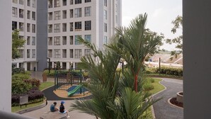 Un edificio residencial con un parque infantil y una palmera en primer plano.