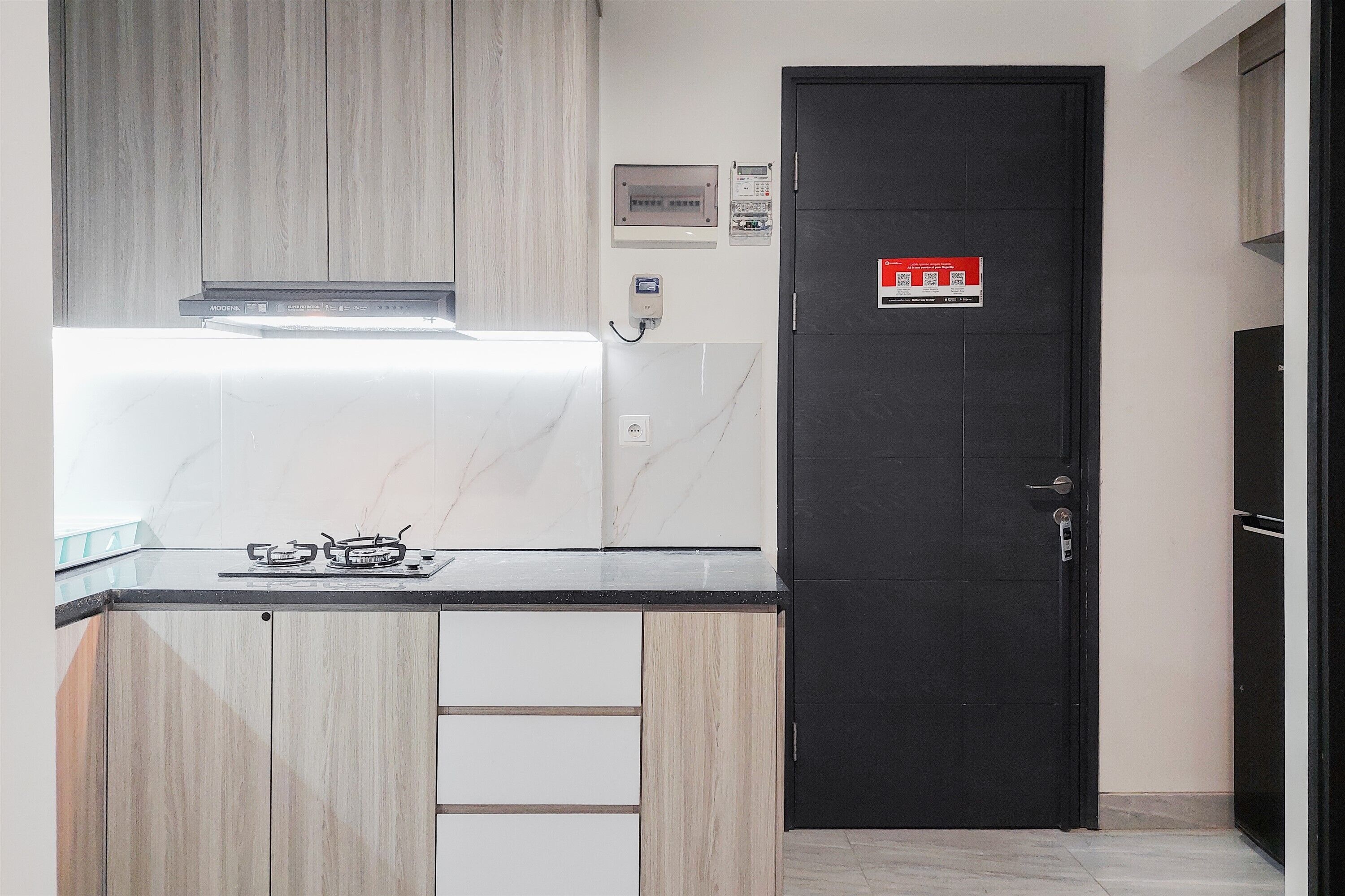 A kitchen with a black door, a stove, and a wall-mounted electrical panel.