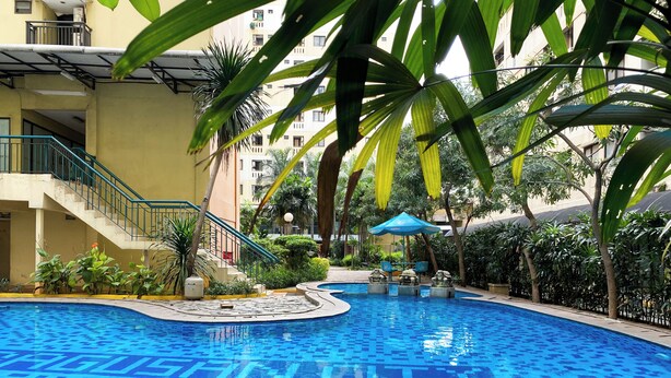 A swimming pool with a tiled pattern, surrounded by greenery and a staircase leading to an upper level. - Good Place 2Br At Kebagusan City Apartment (Jakarta)