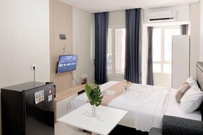 A hotel room with a bed, bedside table, TV, air conditioning unit, and a window with curtains. - Best Furnished And Homey Studio Nifarro Park Apartment (Jakarta)