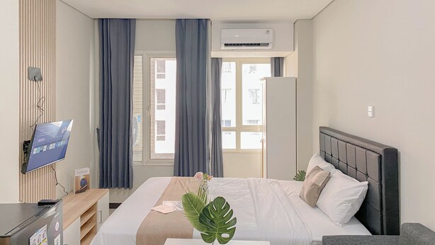 A hotel room with a bed, a desk with a computer, a TV, and a window with curtains. - Best Furnished And Homey Studio Nifarro Park Apartment (Jakarta)