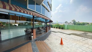 An outdoor seating area with tables and chairs, a green fence, and a view of the cityscape. - Best Furnished And Homey Studio Nifarro Park Apartment (Jakarta)