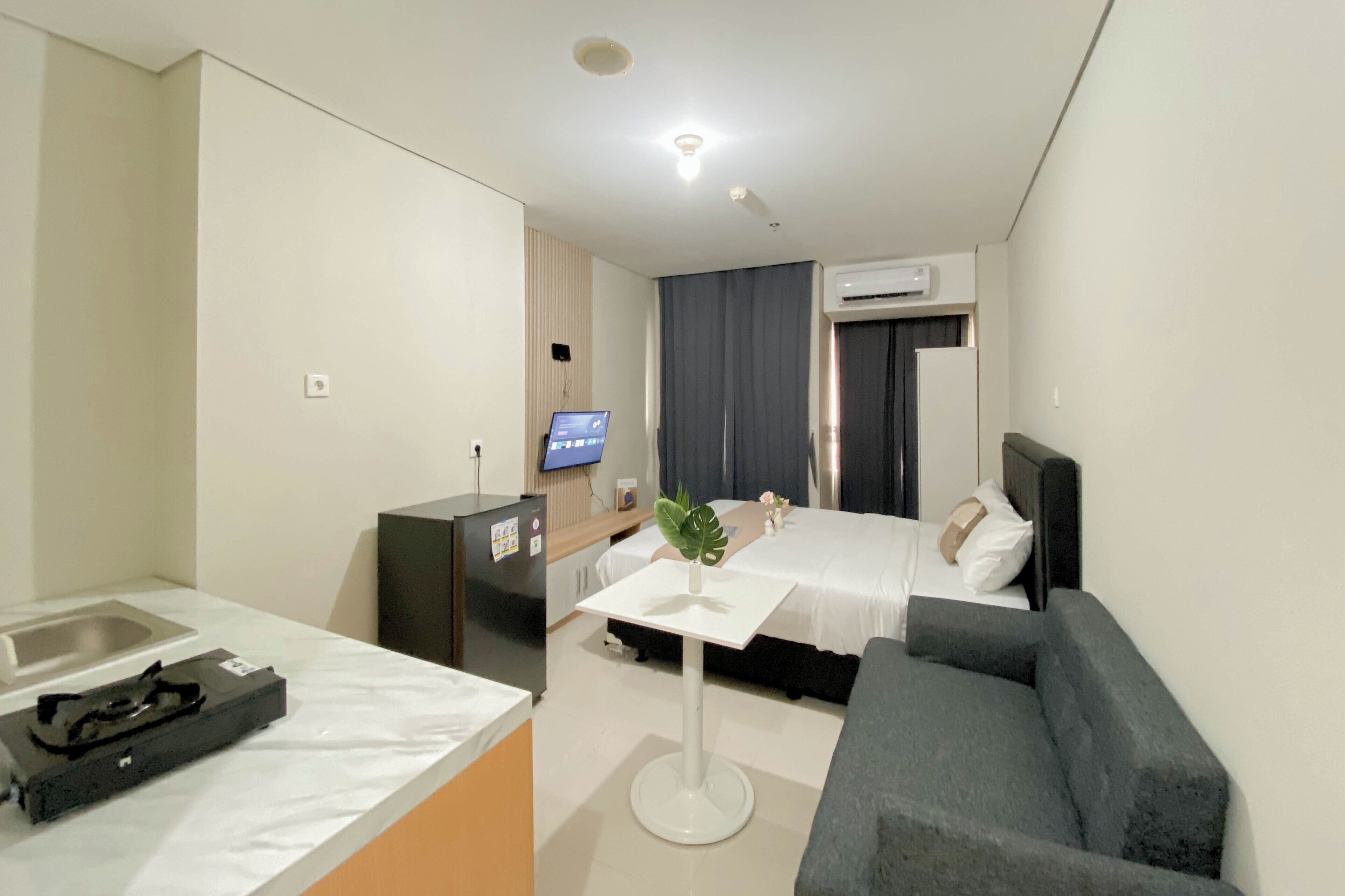 Hotelkamer met een bed, een bureau, een stoel, een klein tafeltje met een plant, een televisie en een airconditioner.