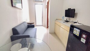 Une chambre d’hôtel moderne avec une table en verre, un canapé, un coin cuisine équipé d’un réfrigérateur et un téléviseur.
