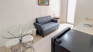 Un salon avec un canapé gris, une table en verre entourée de quatre chaises, une petite table ronde et un meuble noir.
