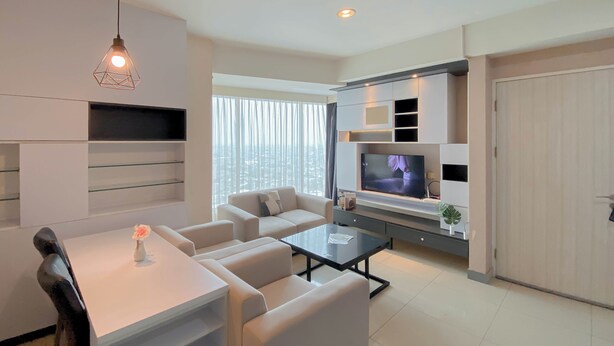 A modern living room with a sofa, coffee table, TV, and a dining area with chairs and a table. - Nice And Elegant 2Br At Grand Kamala Lagoon Apartment (Bekasi)