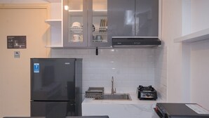 Una cucina compatta con frigorifero nero, lavello, piano cottura e lavastoviglie. Sopra il lavello ci sono pensili e un piccolo angolo con tavolo e sedie.