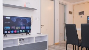 Un soggiorno moderno con una TV a schermo piatto che mostra una trasmissione, un mobile TV bianco e una zona pranzo con sedie nere.