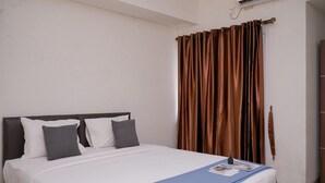 A neatly made bed with white and gray bedding, a blue throw blanket, and a small table with a remote control and a magazine.
